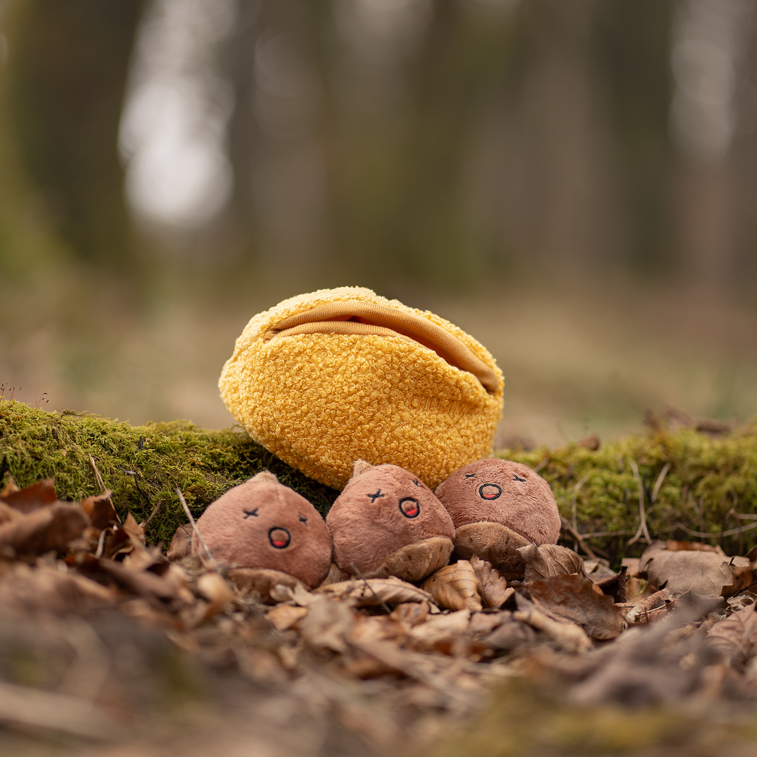 Yellow plush bag with small brown plush toys on a forest floor