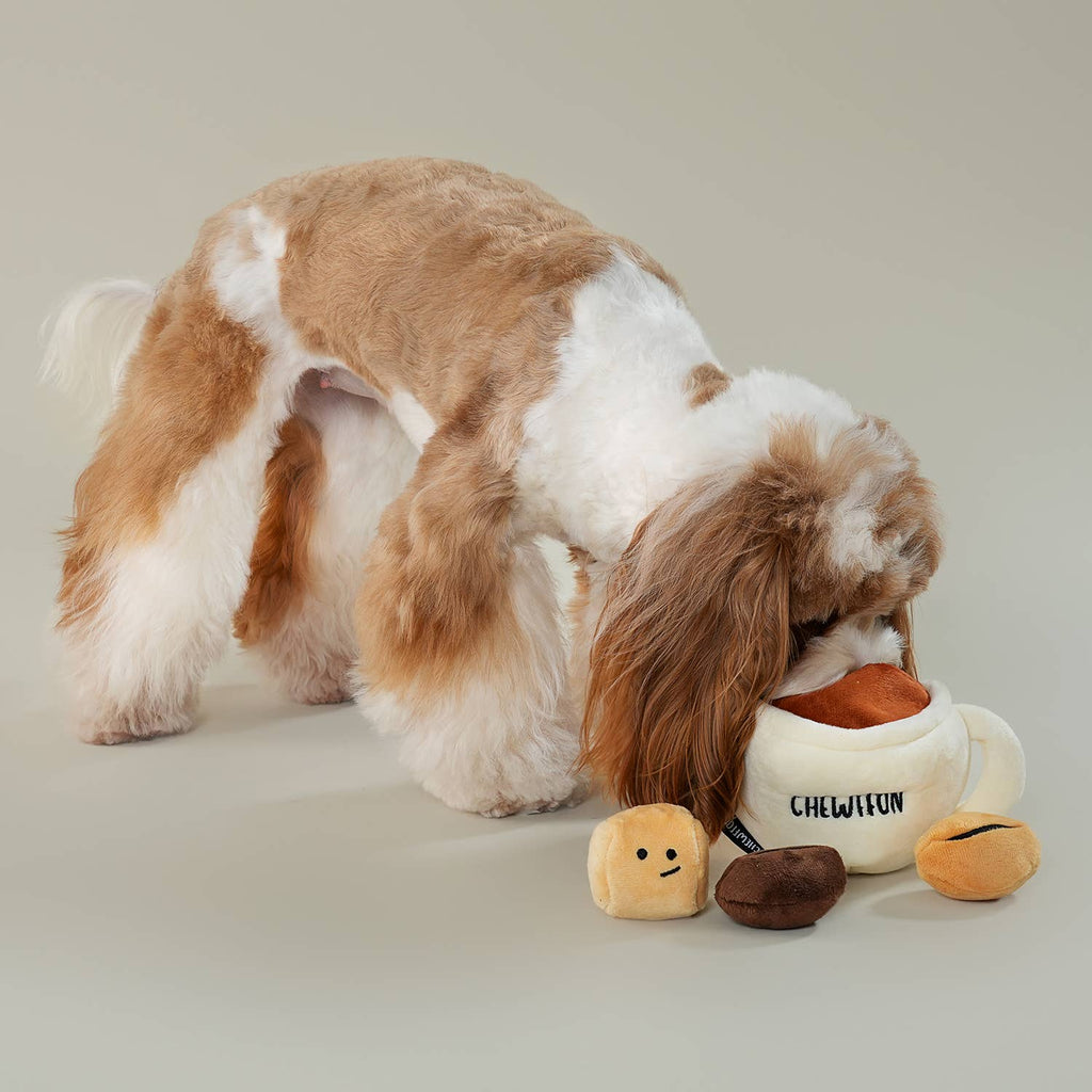 Dog playing with a chew toy shaped like a teacup with a duck inside on a neutral background